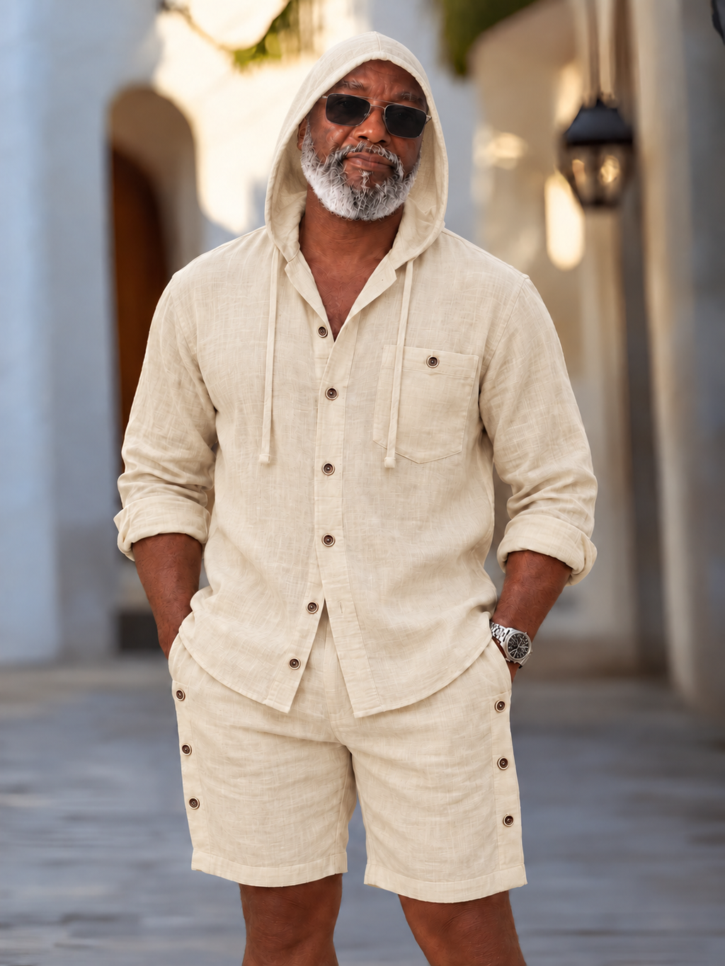 Model wearing cream hooded button-front shirt and matching shorts with hood up and sunglasses